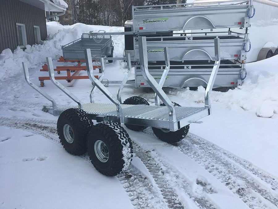 Une remorque avec des bûches dessus est garée dans la neige.