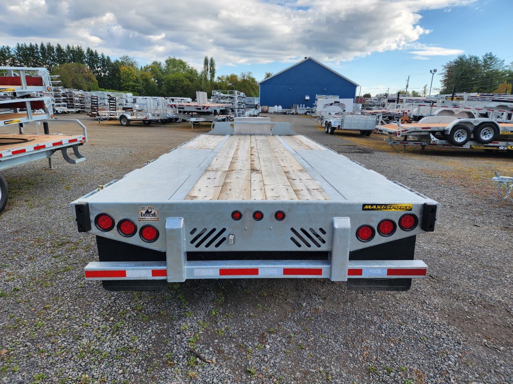Une remorque est garée sur un terrain en gravier devant un bâtiment.