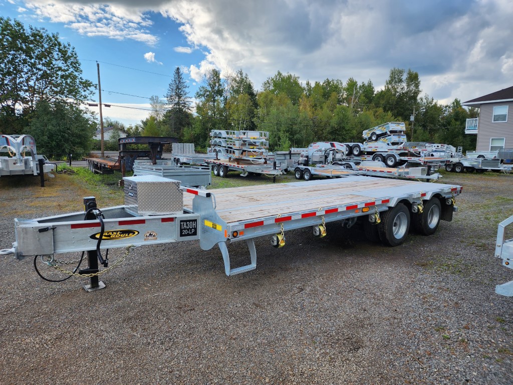 Une remorque à plateau est garée sur un terrain en gravier.