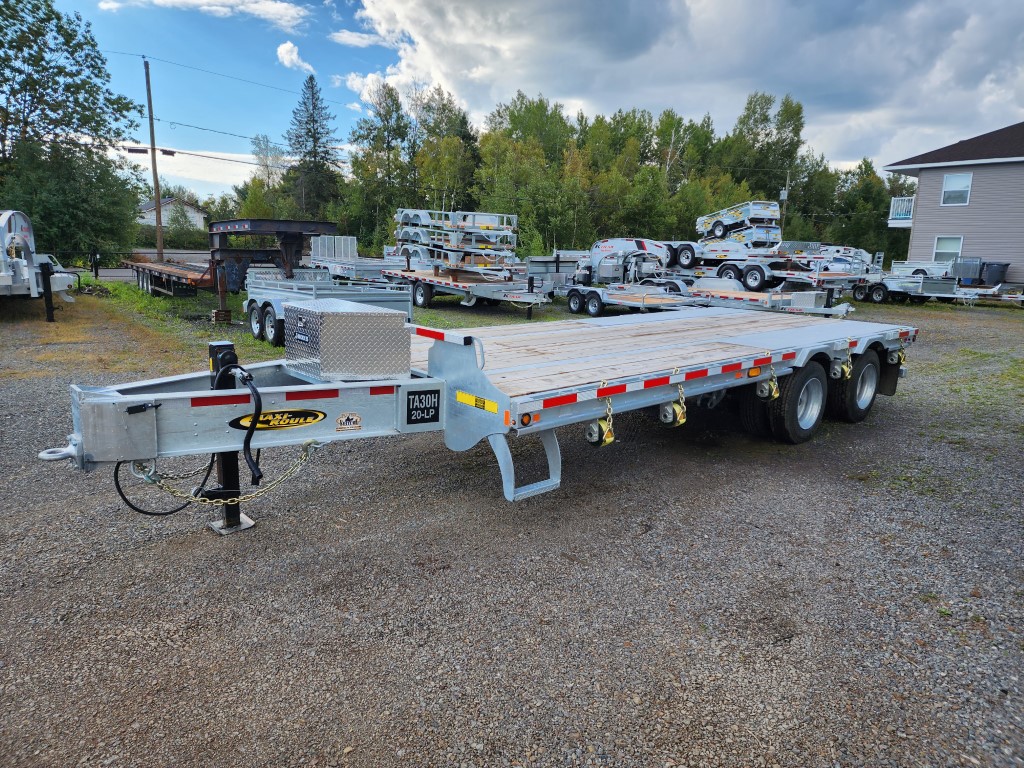 Une remorque à plateau est garée sur un terrain en gravier.