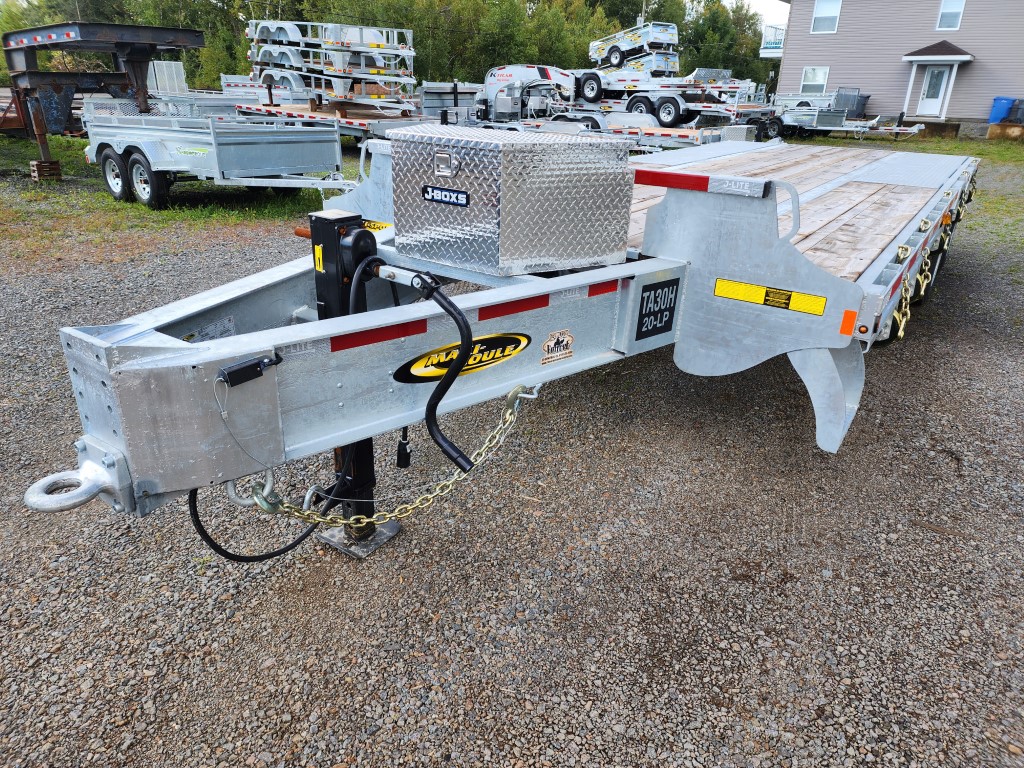 Une remorque à plateau est garée sur un terrain en gravier.