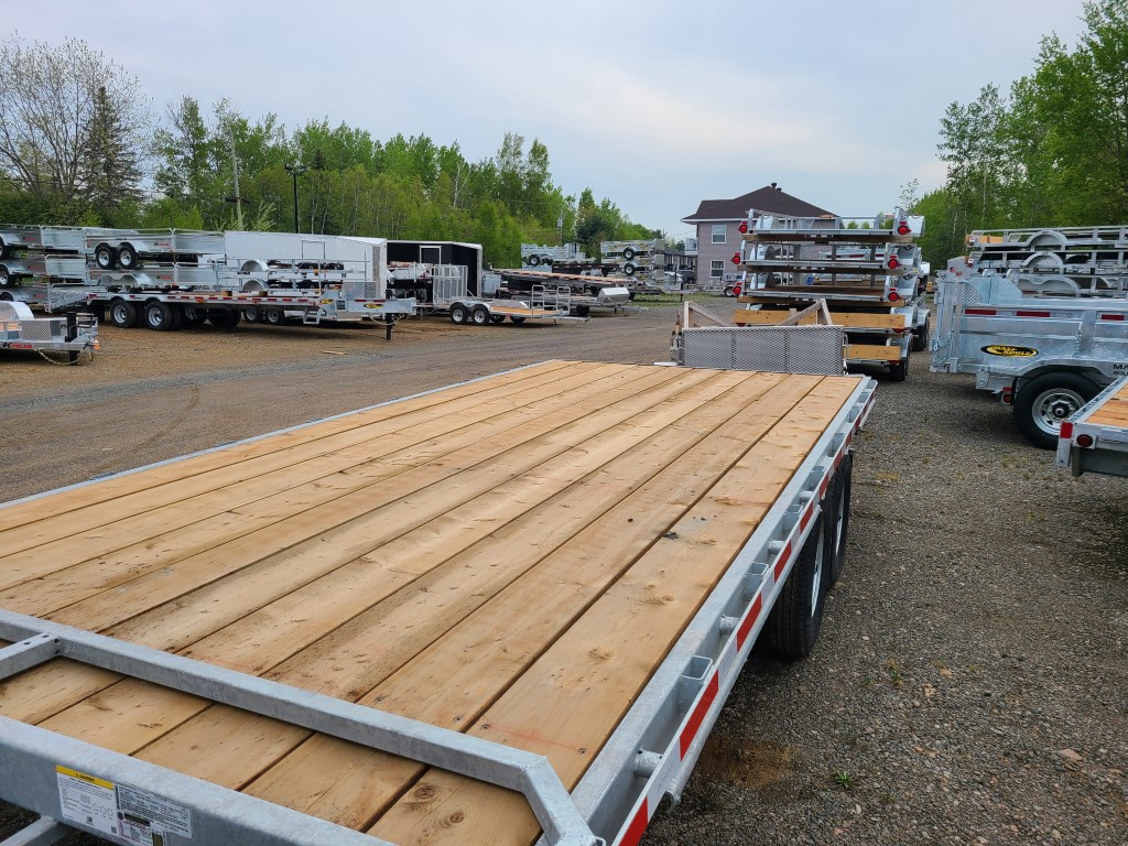 Une remorque avec une terrasse en bois est garée sur un terrain en gravier.