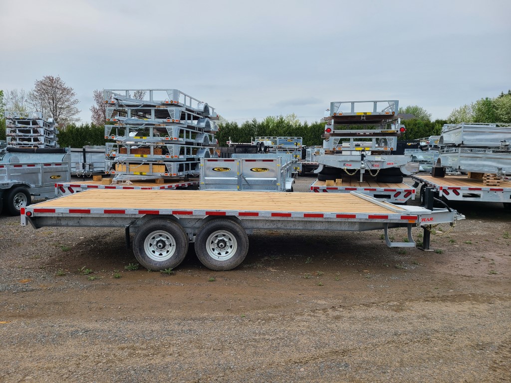 Une remorque à plateau est garée sur un terrain en gravier.