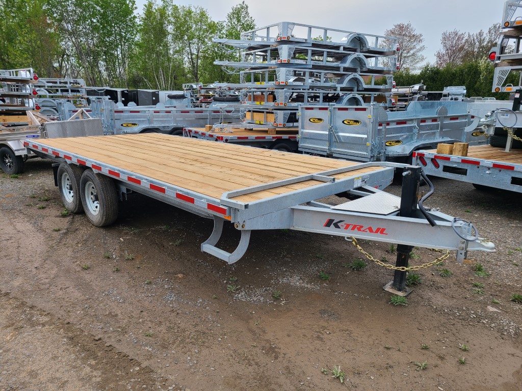 Une remorque à plateau est garée sur un terrain en terre.