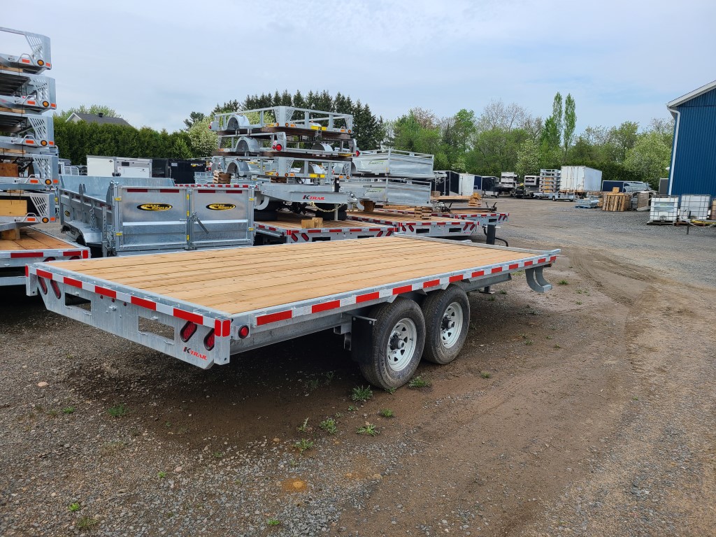 Une remorque avec une terrasse en bois est garée sur un terrain en terre.