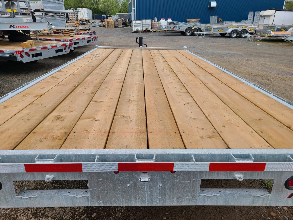 Une remorque avec un pont en bois est garée dans un parking.