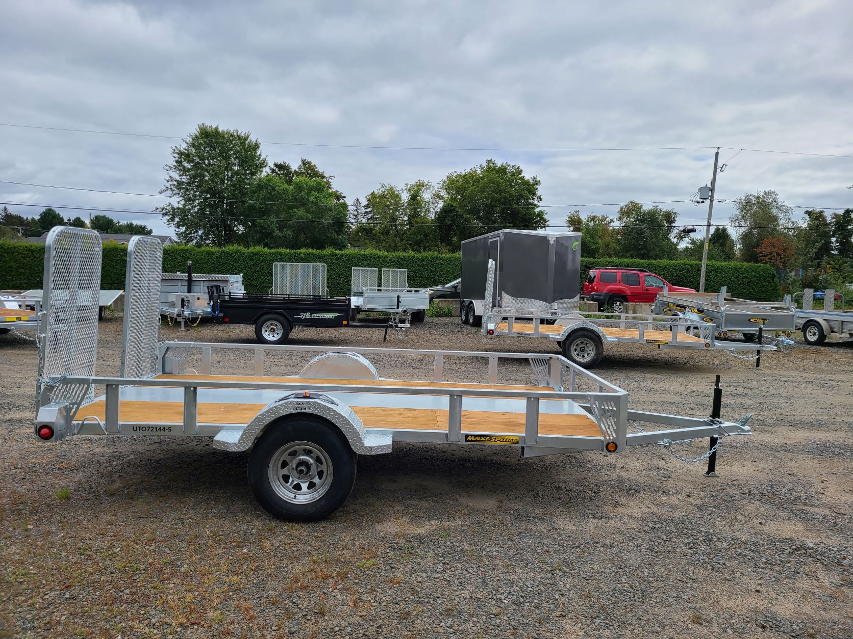 Une remorque avec une terrasse en bois est garée sur un terrain en gravier.
