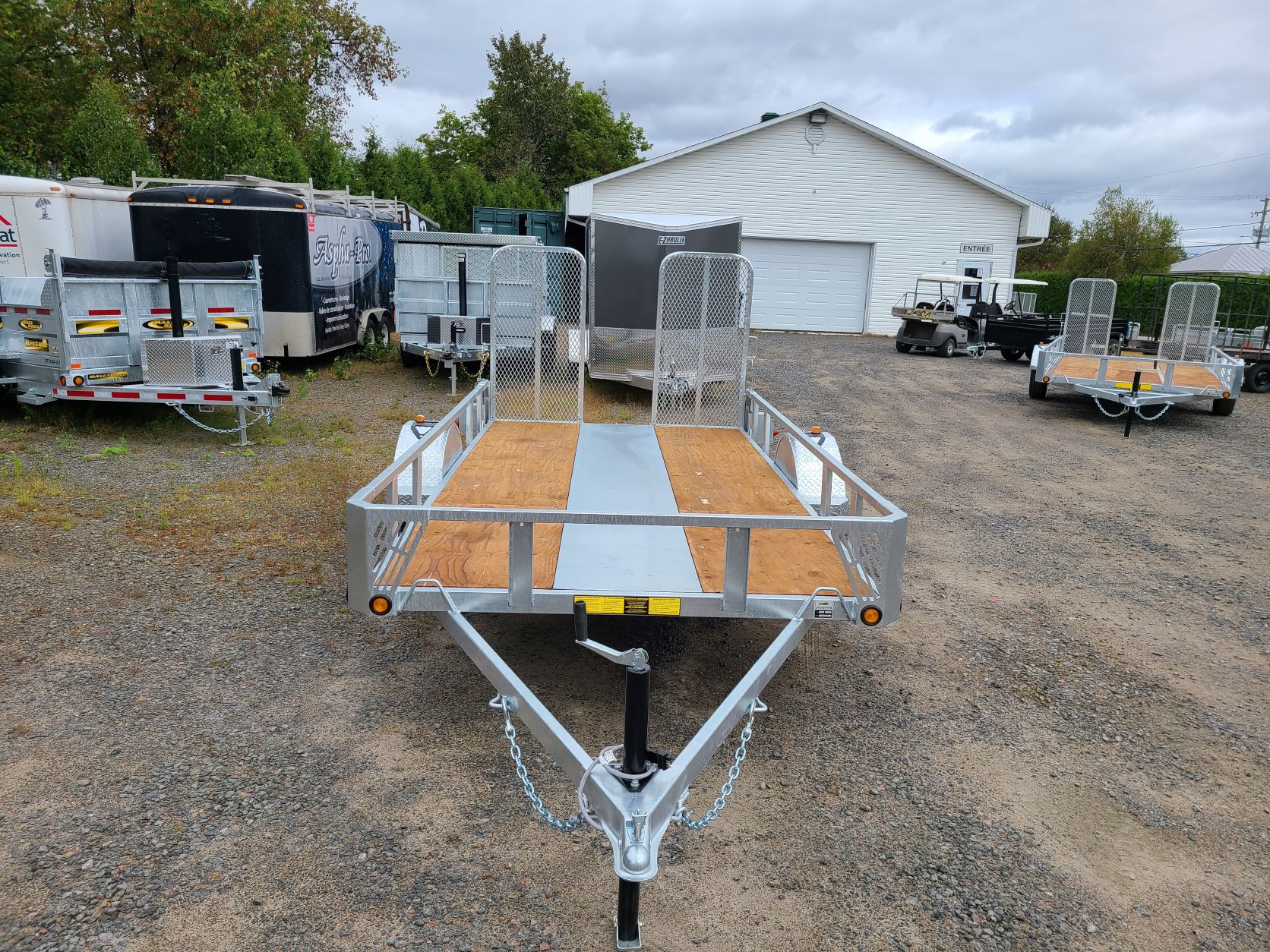 Une remorque est garée sur un terrain en gravier devant un garage.