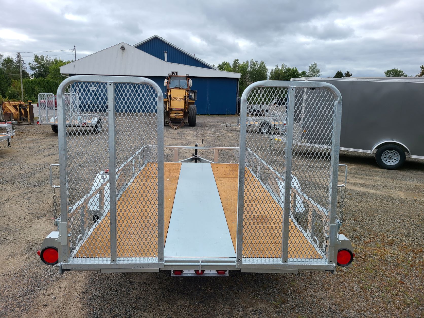 Une remorque est garée sur un terrain en gravier avec un tracteur en arrière-plan