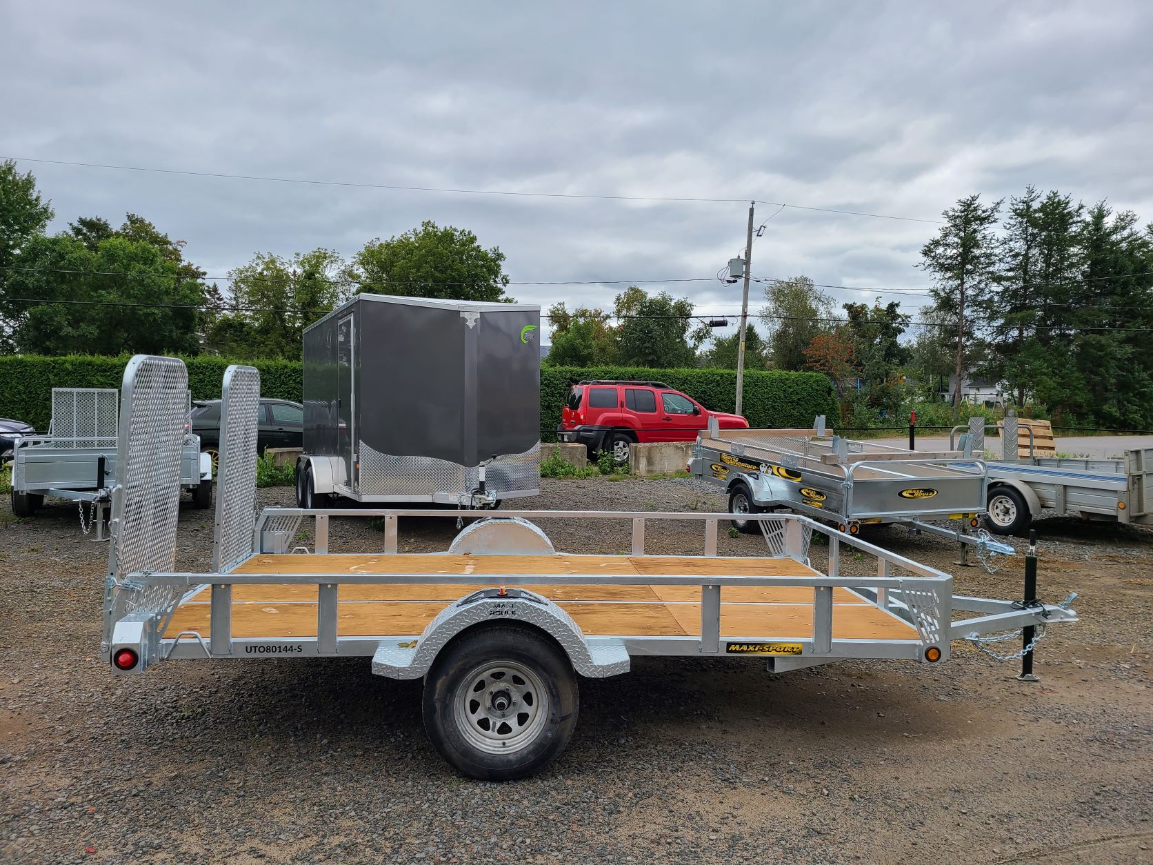 Une remorque avec une terrasse en bois est garée sur un terrain en gravier.