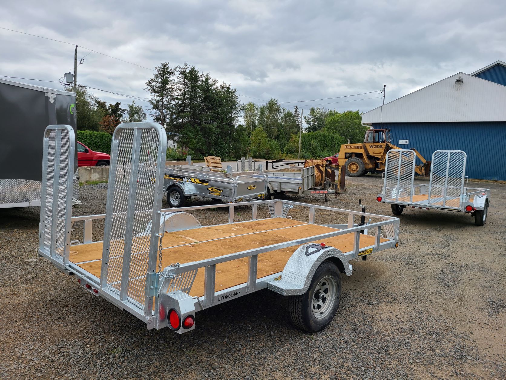 Deux remorques sont garées sur un terrain en gravier devant un bâtiment.