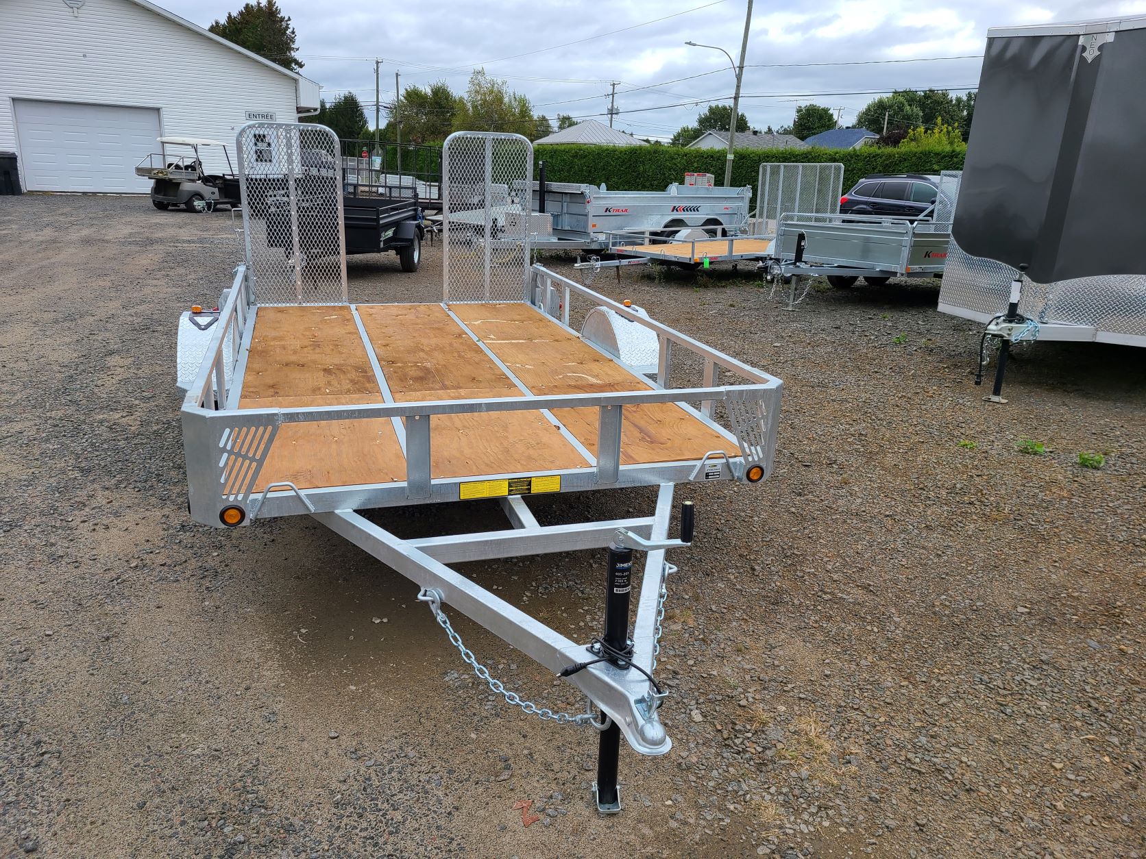 Une remorque avec une terrasse en bois est garée sur un terrain en gravier.