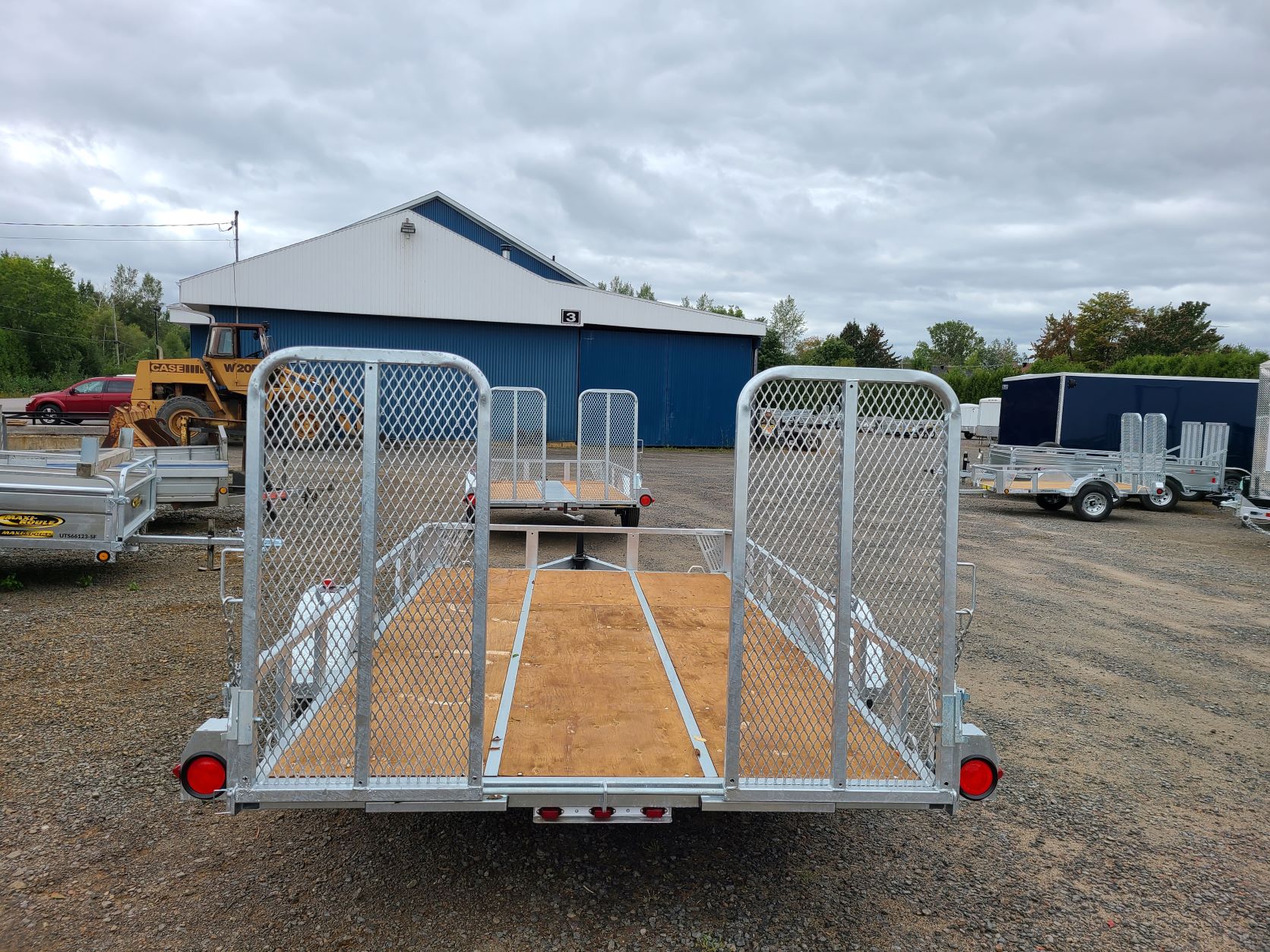 Une remorque est garée sur un terrain en gravier devant un bâtiment.