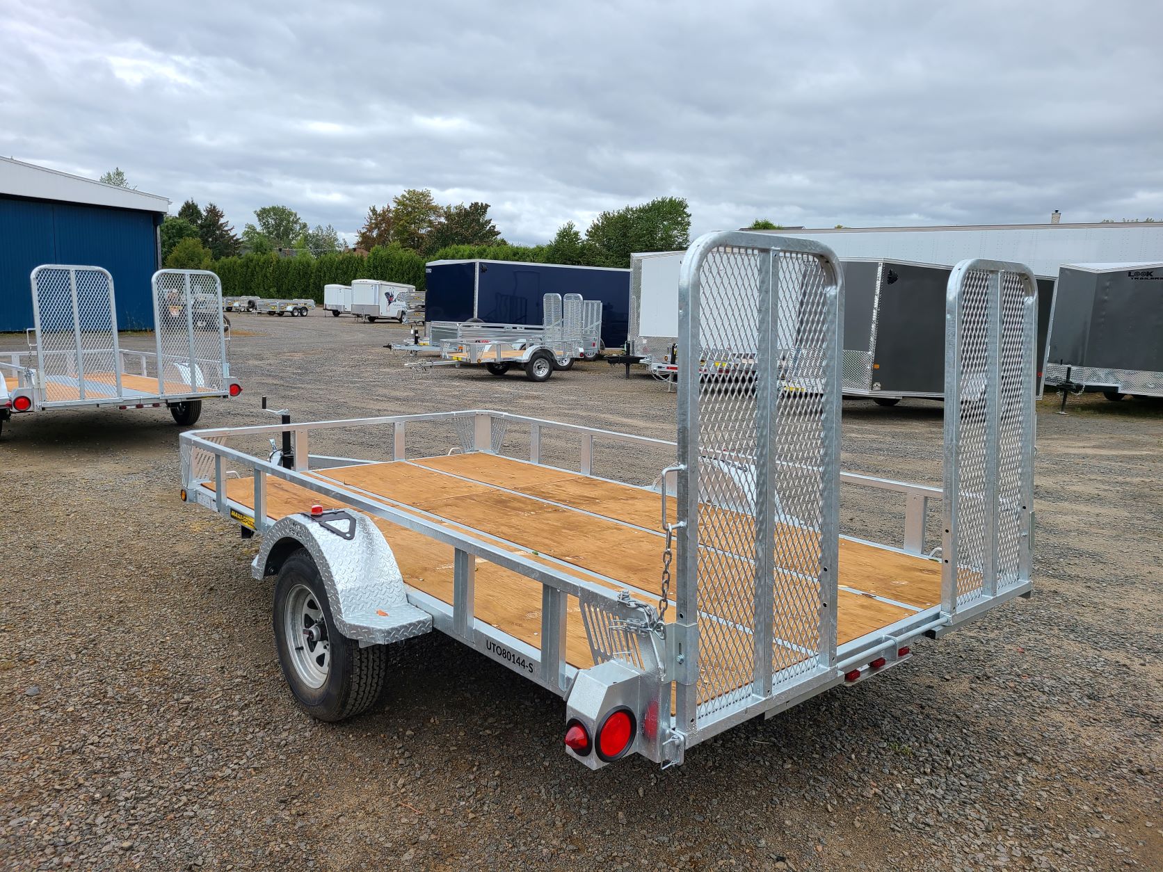 Une remorque avec une terrasse en bois est garée sur un terrain en gravier.