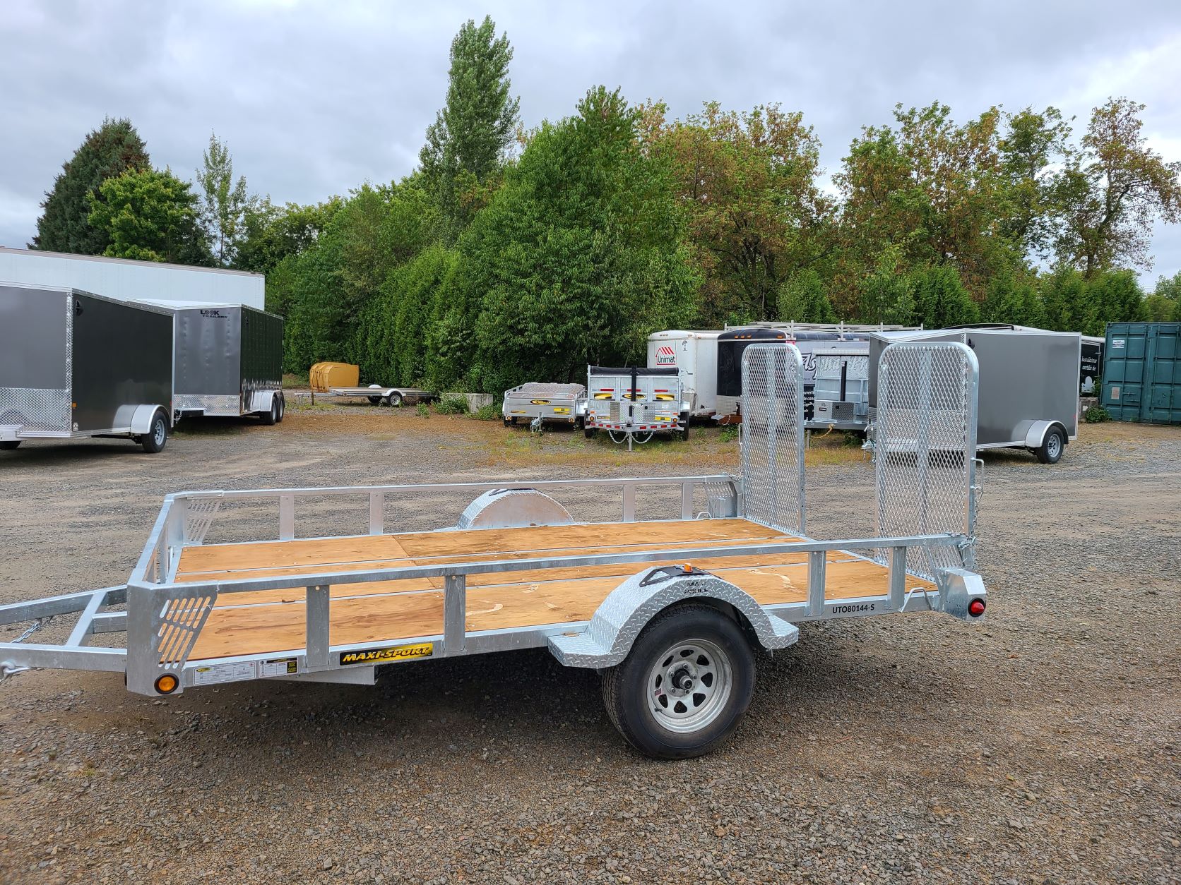 Une remorque avec une terrasse en bois est garée sur un terrain en gravier.