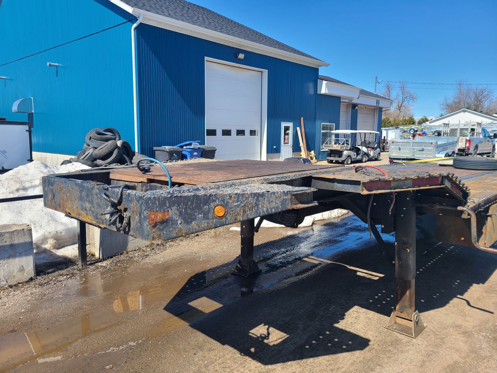 Une remorque à plateau est garée devant un bâtiment bleu.