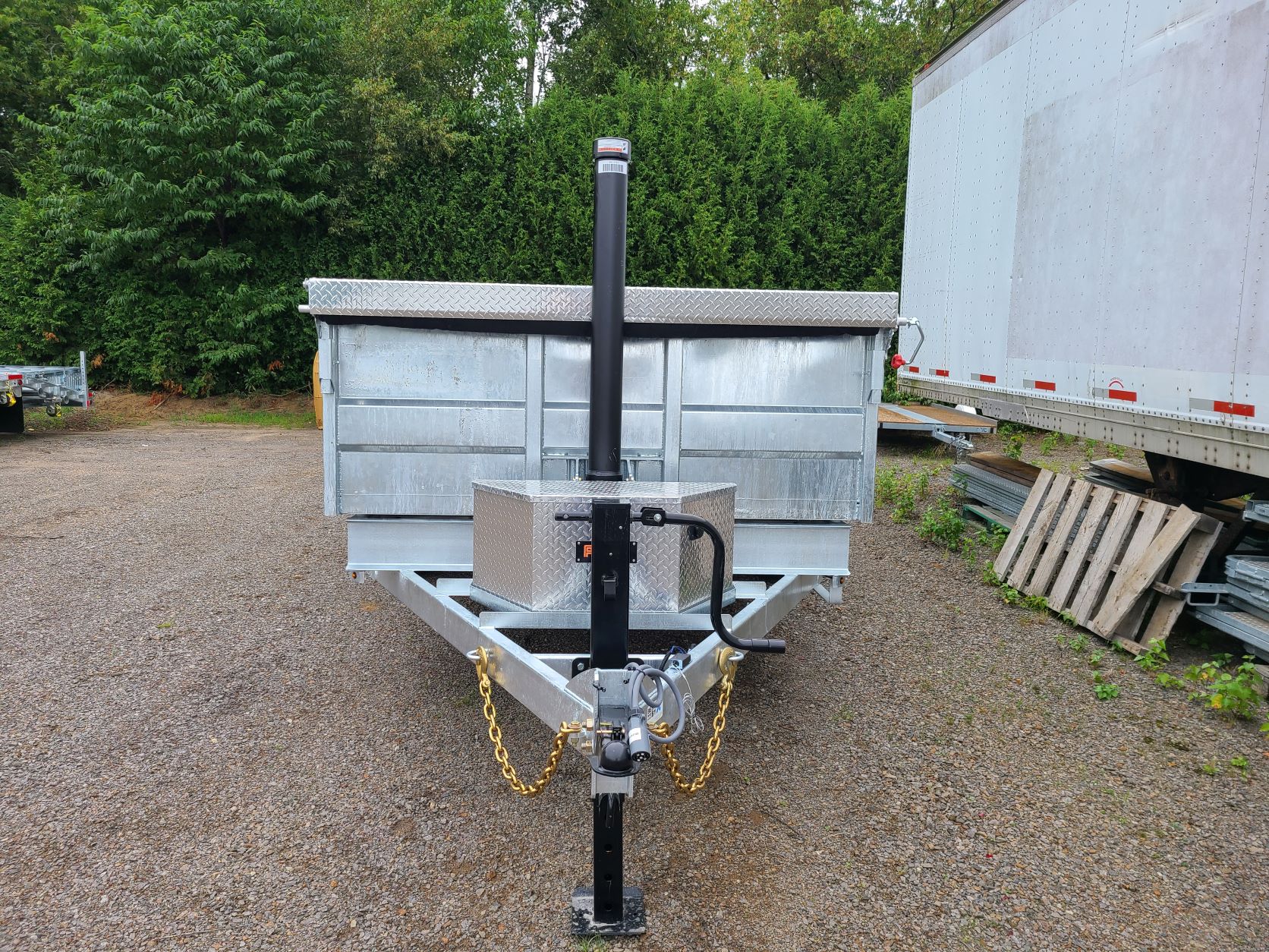 Une remorque est garée sur un terrain en gravier à côté d'une remorque blanche.