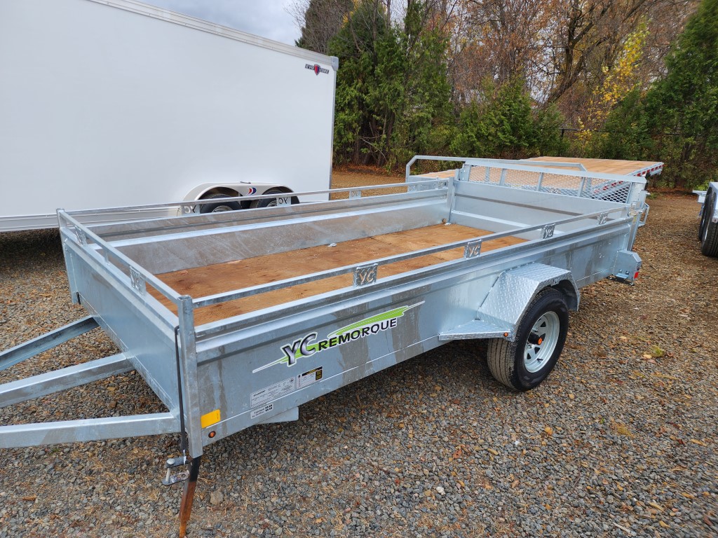 Une remorque est garée sur un terrain en gravier à côté d'une remorque blanche.