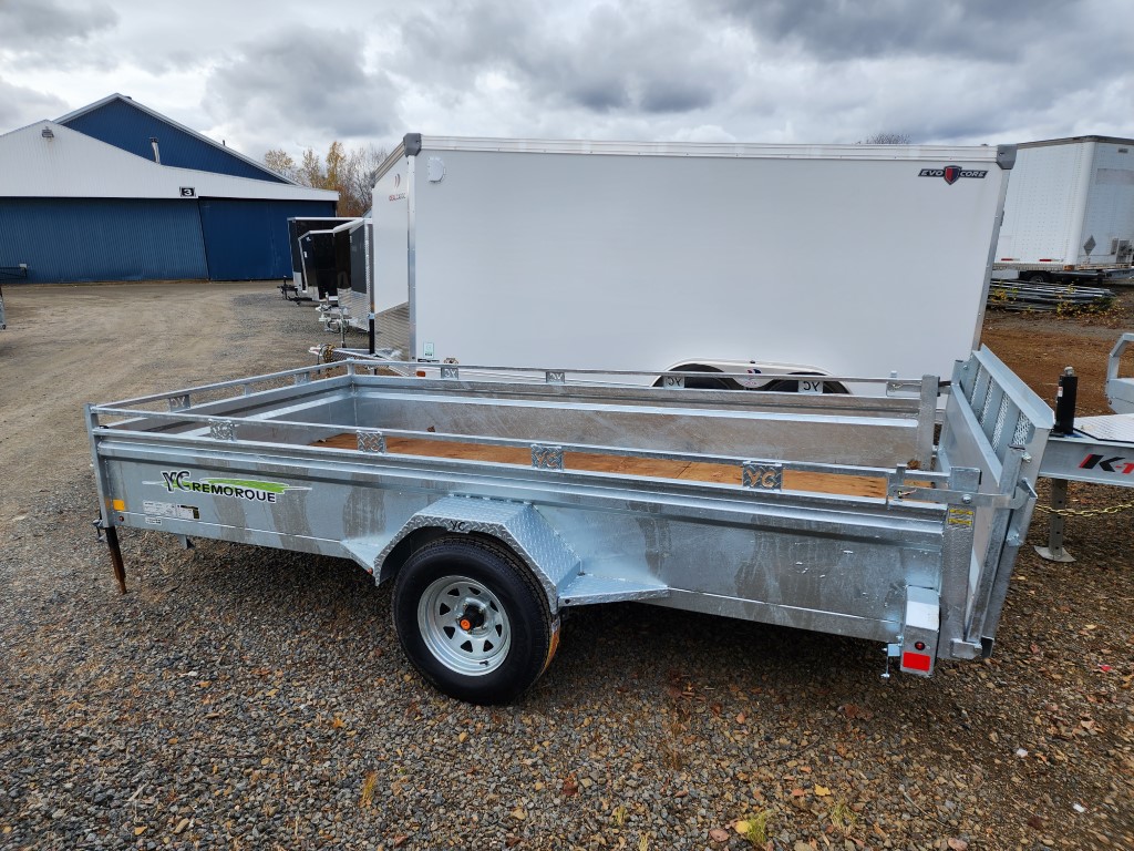 Une remorque avec une boîte blanche dessus est garée sur un terrain en gravier.