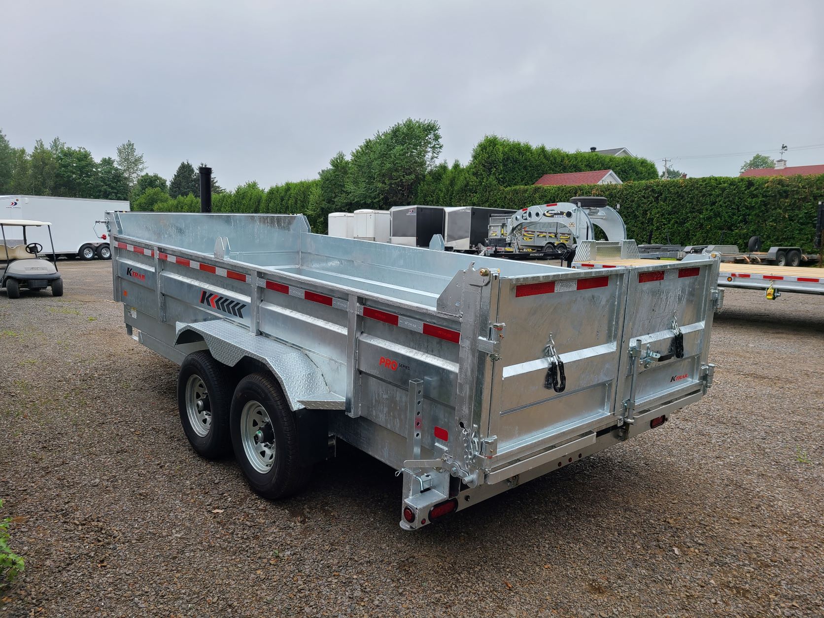 Une remorque à benne basculante est garée sur un terrain en gravier.