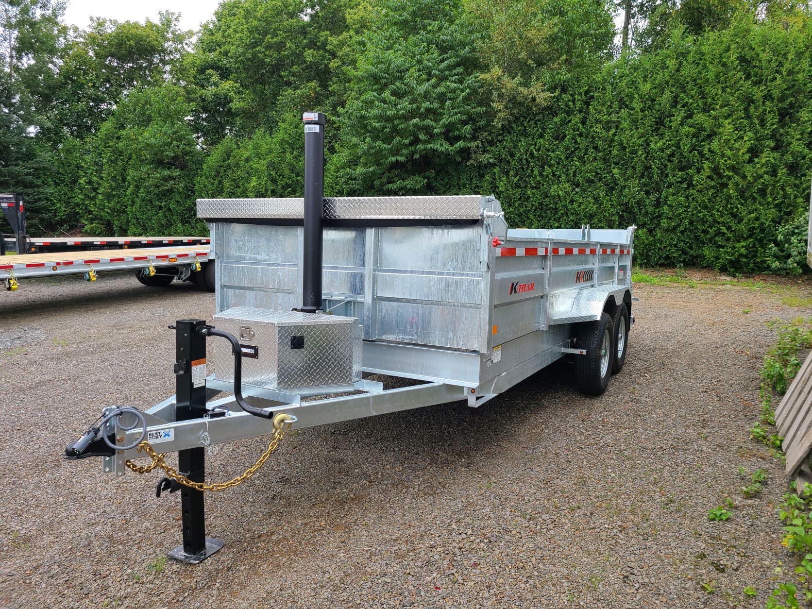 Une remorque à benne basculante est garée sur un terrain en gravier.