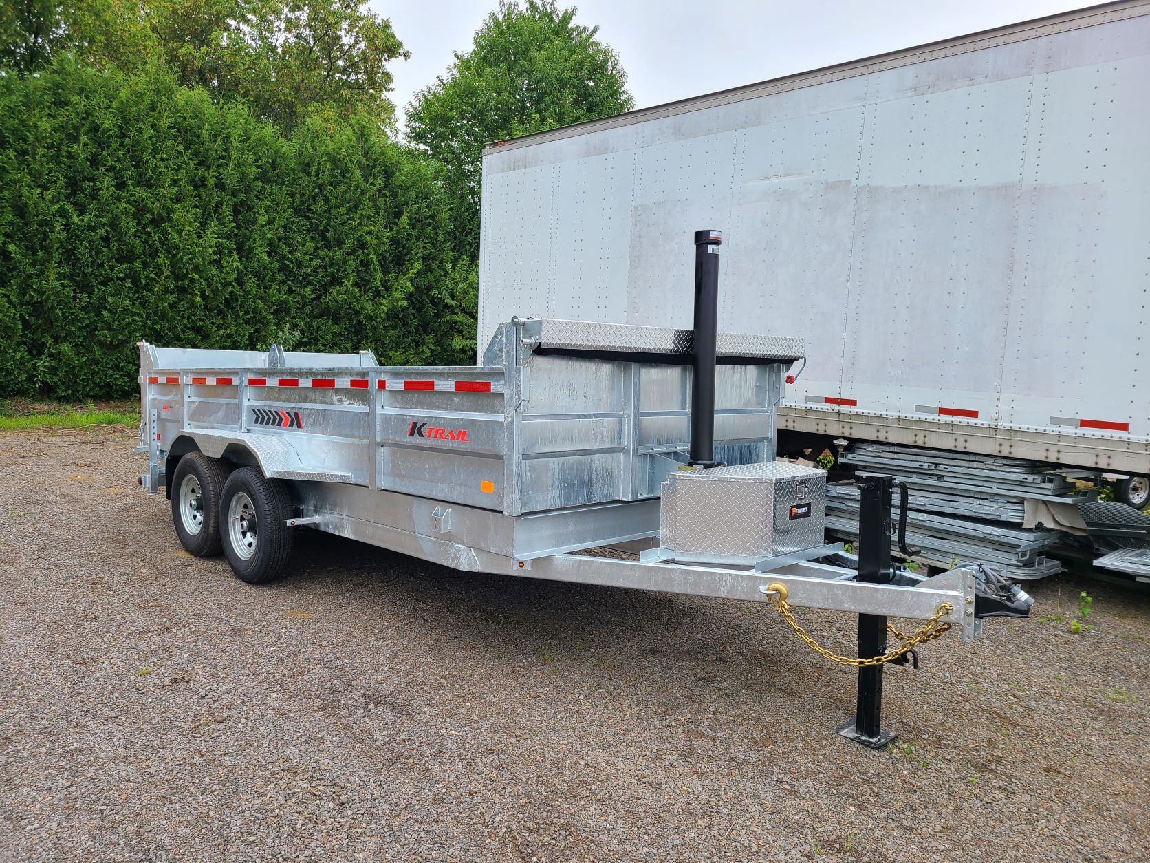 Une remorque est garée sur un terrain en gravier à côté d'une remorque blanche.