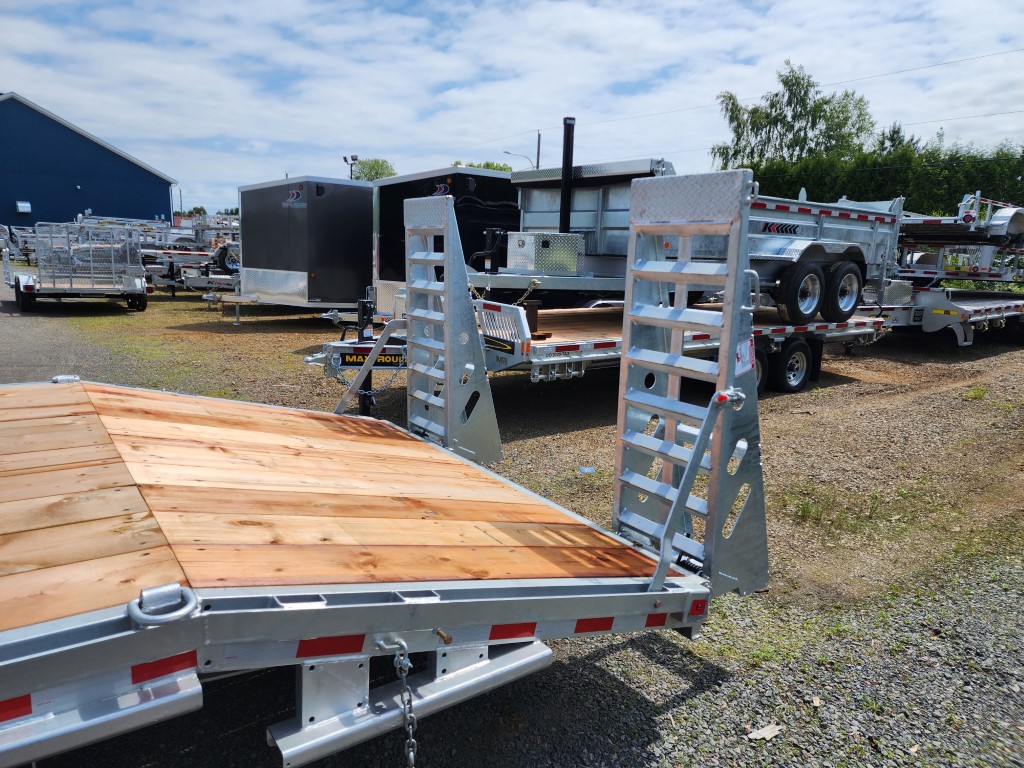 Une remorque avec une terrasse en bois est garée sur un terrain en gravier.