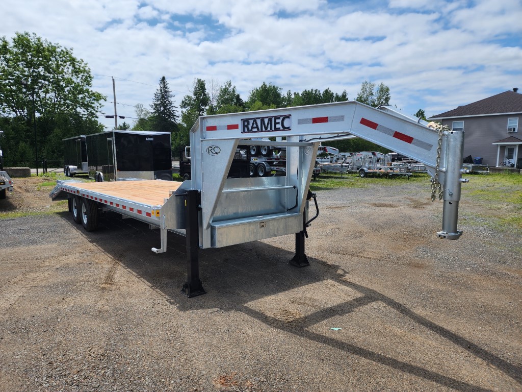 Une remorque à plateau est garée sur un terrain en gravier.