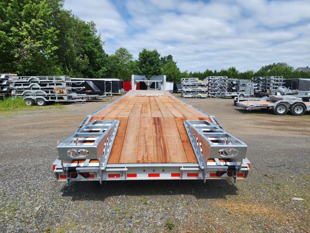 Une remorque avec une terrasse en bois est garée sur un terrain en gravier.