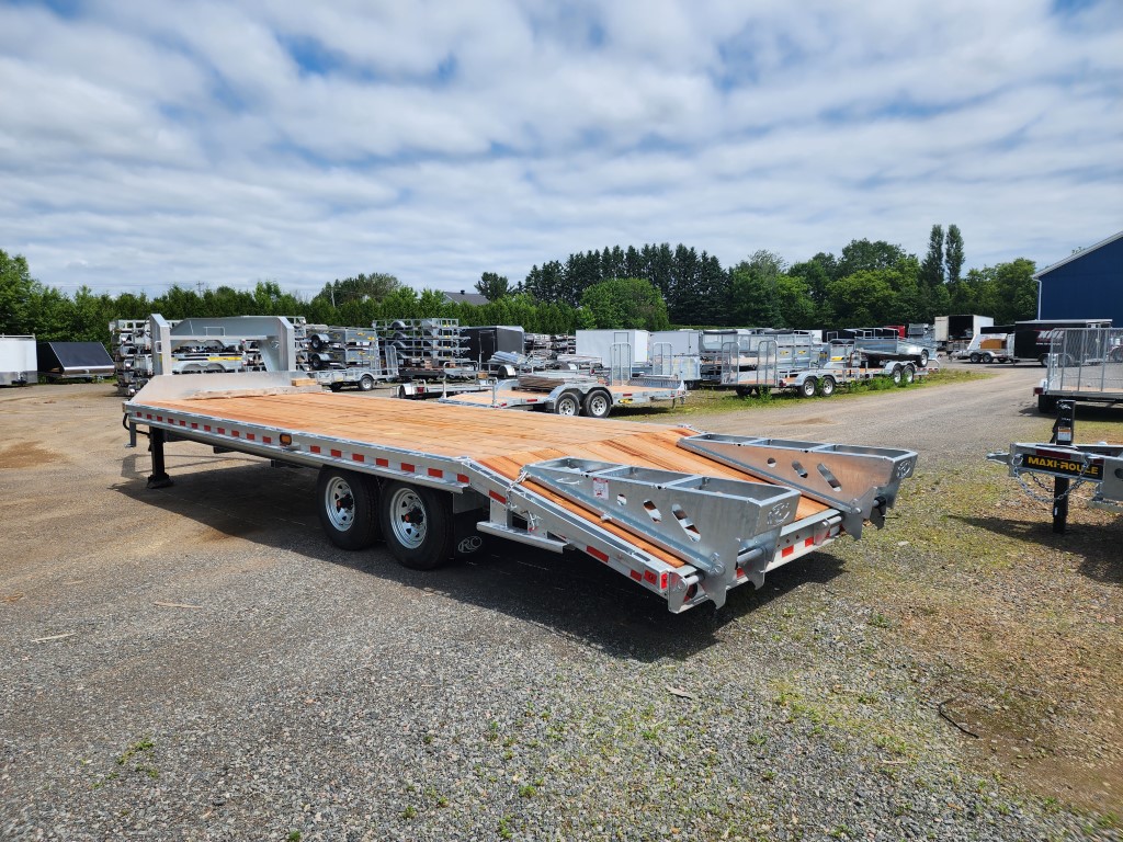 Une remorque à plateau est garée sur un terrain en gravier.