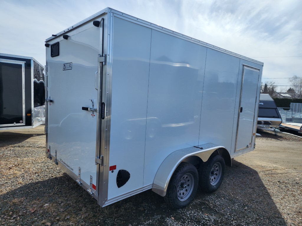 Une remorque blanche est garée sur un terrain en gravier.