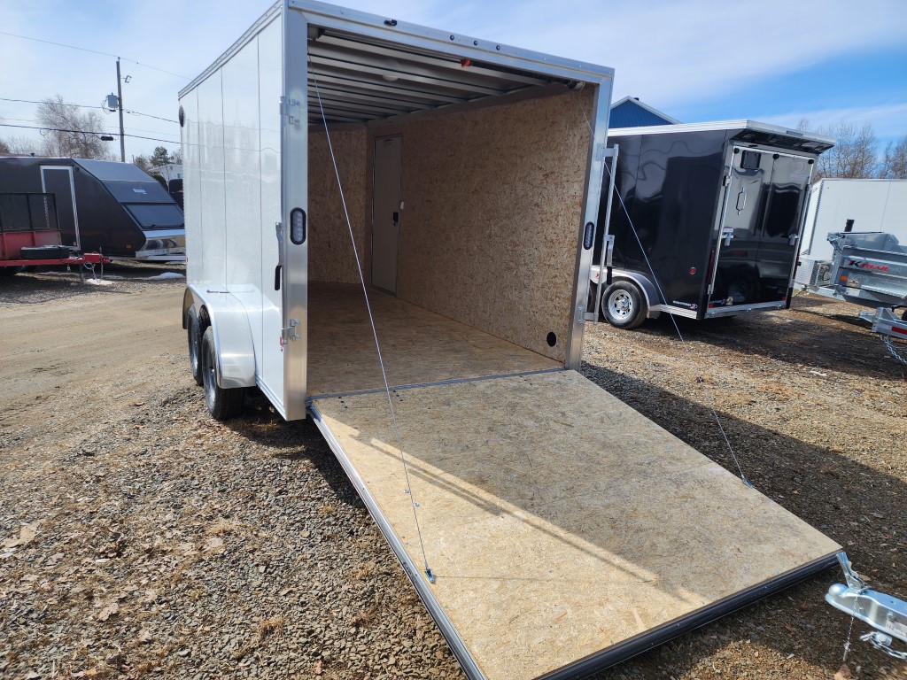 Une remorque blanche avec la porte ouverte est garée sur un terrain en gravier.