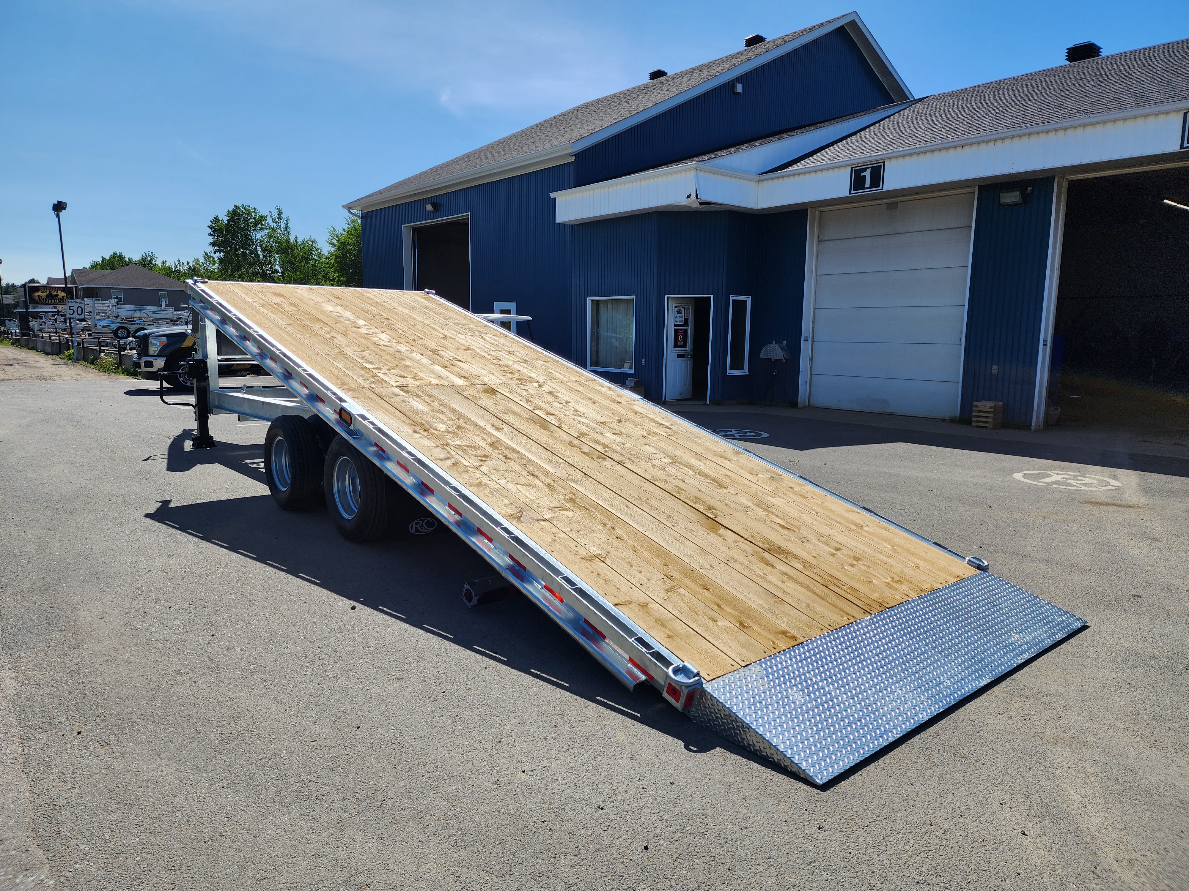 Une remorque à plateau est garée devant un bâtiment bleu.