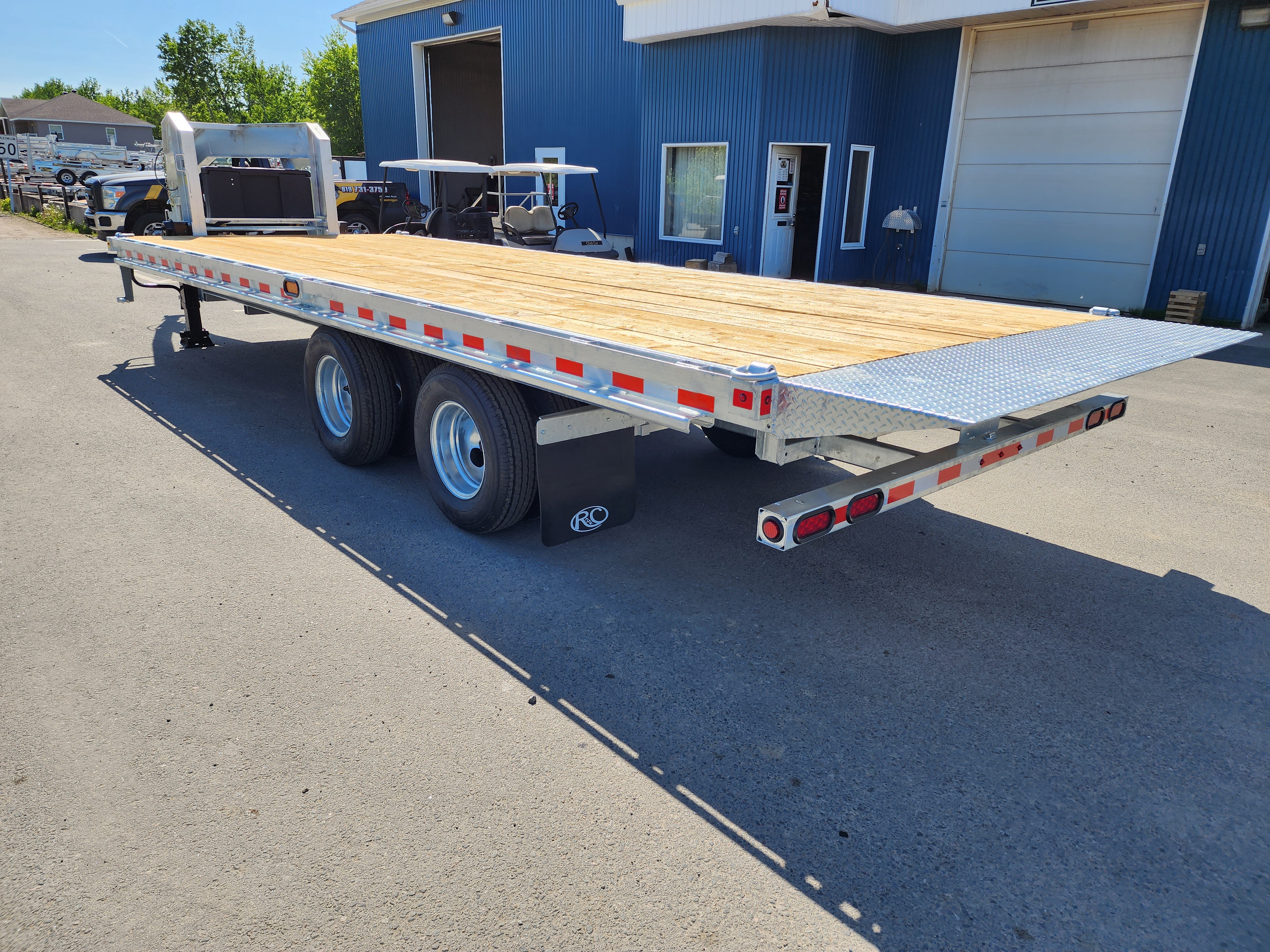 Une remorque à plateau est garée devant un bâtiment bleu.