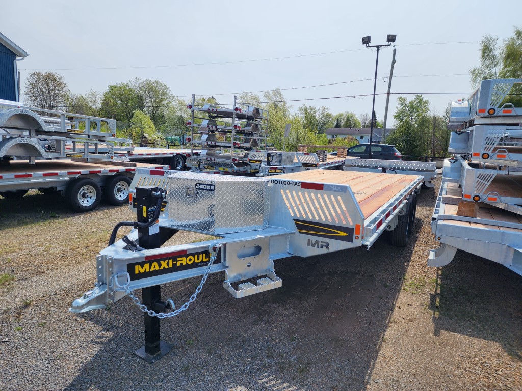 Une remorque à plateau est garée sur un terrain en gravier.