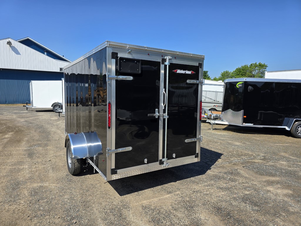 Une remorque noire est garée à côté d'une remorque blanche dans un parking.