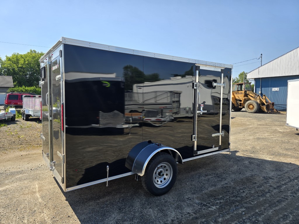 Une remorque noire est garée sur un parking à côté d'un bâtiment.