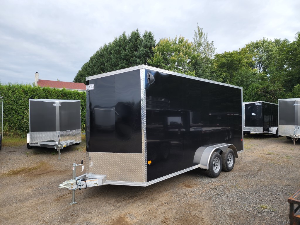 Une remorque noire est garée sur un terrain en gravier