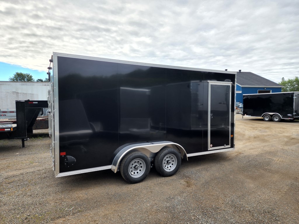 Une remorque noire est garée sur un terrain en gravier.