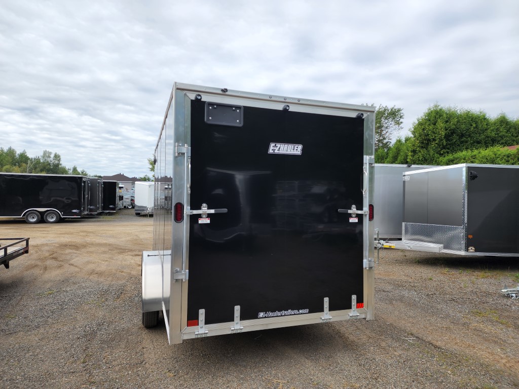 Une remorque noire est garée sur un terrain en gravier.