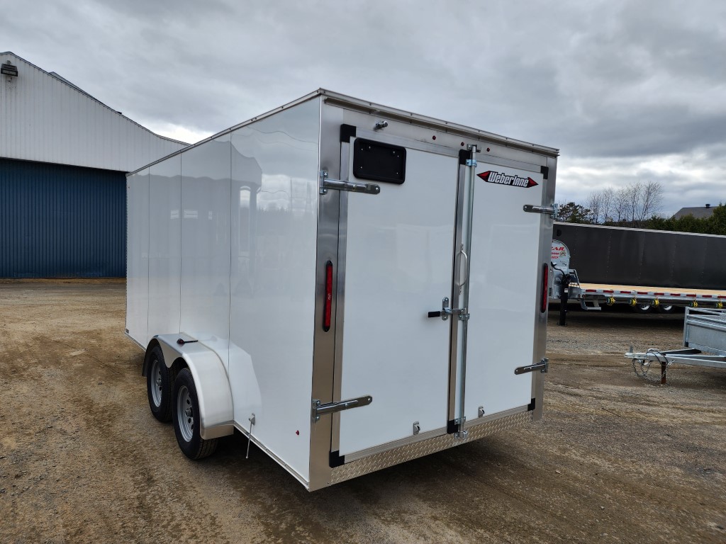 Une remorque blanche est garée sur un terrain en terre devant un bâtiment.