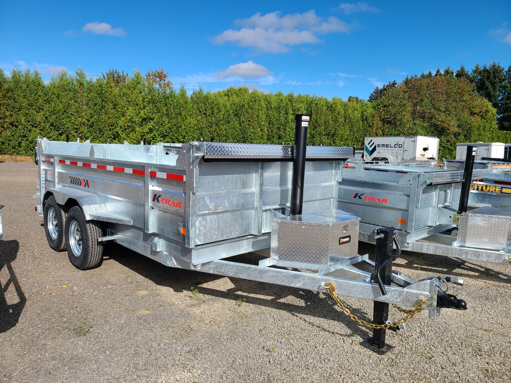 Une remorque à benne basculante est garée sur un terrain en gravier.