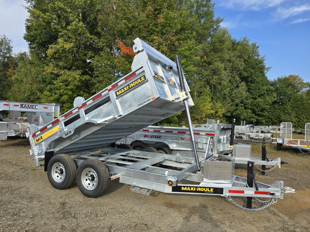 Une remorque à benne basculante est garée sur un terrain avec des arbres en arrière-plan.
