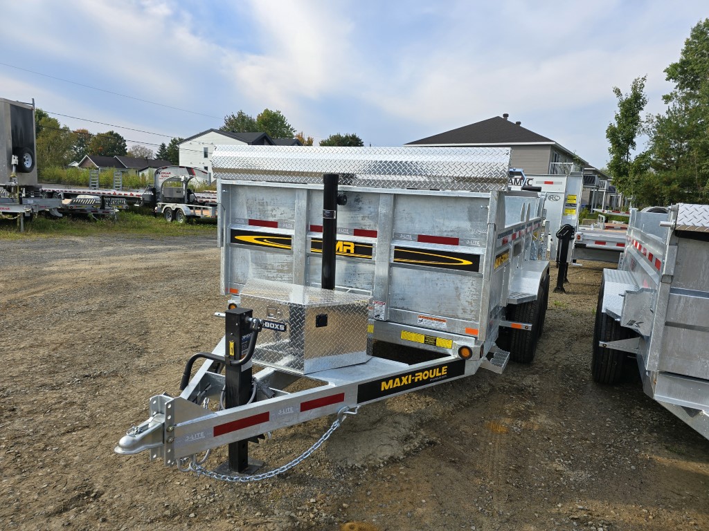 Une remorque à benne basculante est garée sur un terrain en terre.