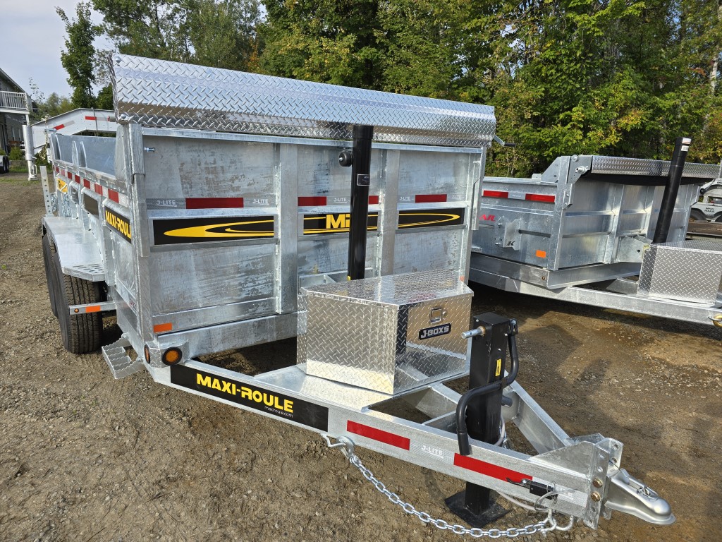 Une remorque à benne basculante est garée sur un terrain en terre.