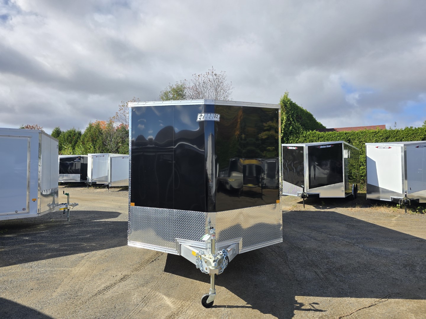 Une remorque noire est garée sur un parking à côté d'une rangée de remorques blanches.