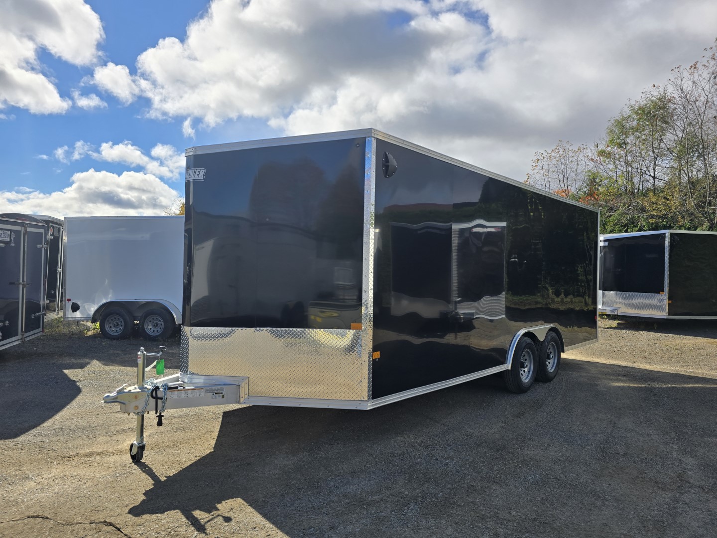 Une remorque noire est garée sur un parking à côté d'une remorque blanche.