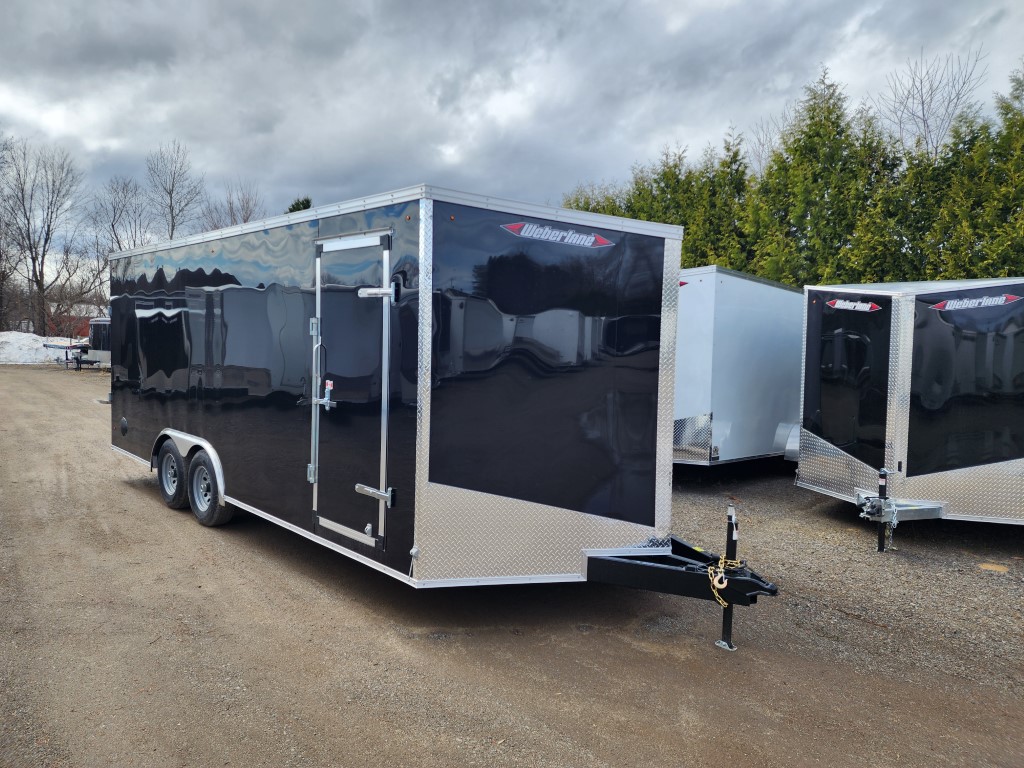Une remorque noire et argentée est garée sur un terrain en gravier.