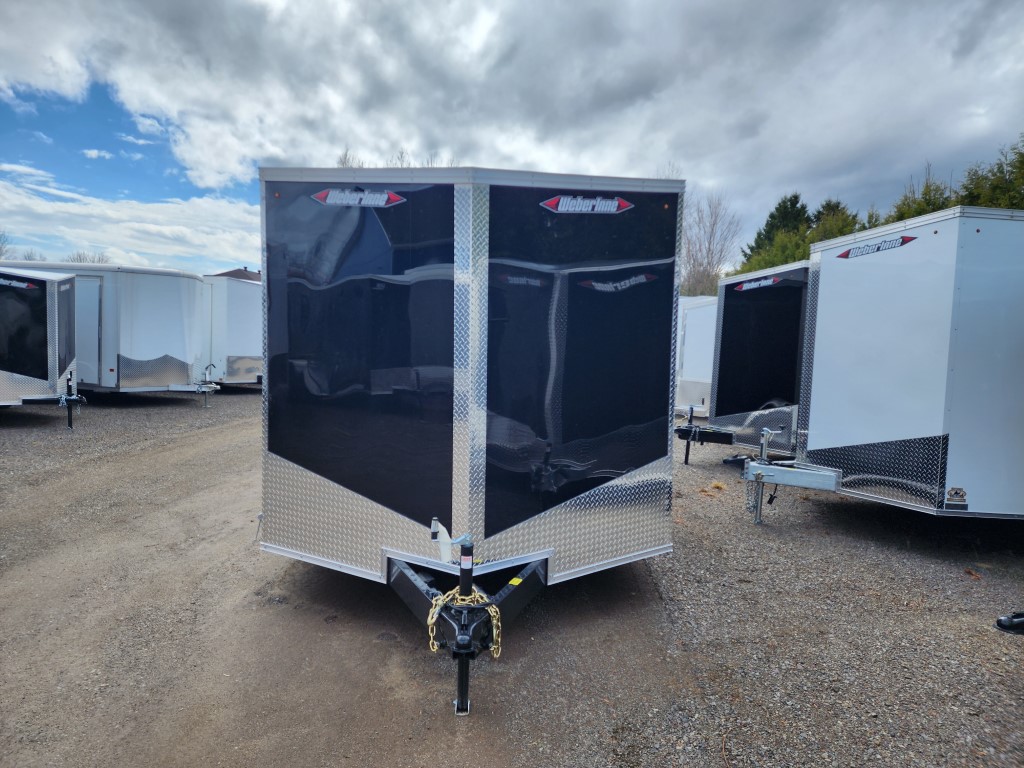 Une remorque noire et argentée est garée sur un terrain en gravier.