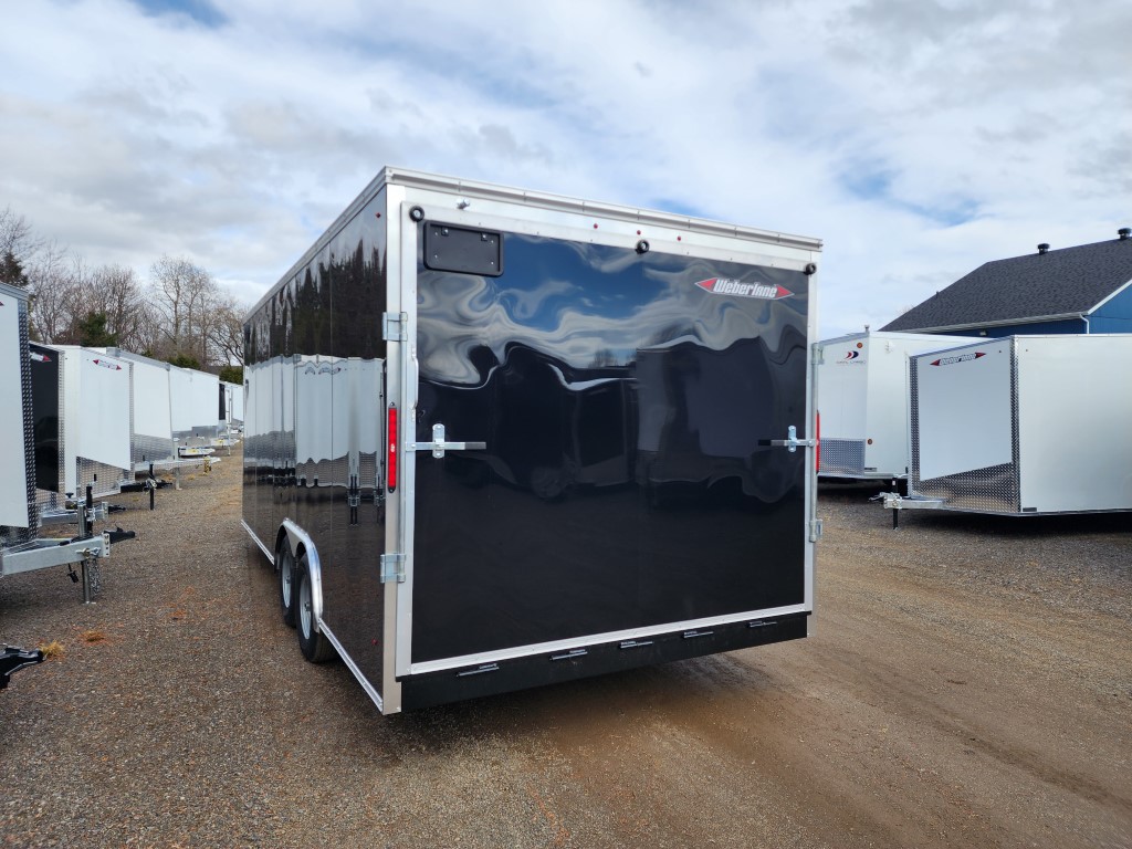 Une remorque noire est garée sur un terrain en gravier à côté d'une maison.